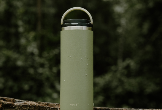 Purist stainless Green water bottle on a log with a forest background