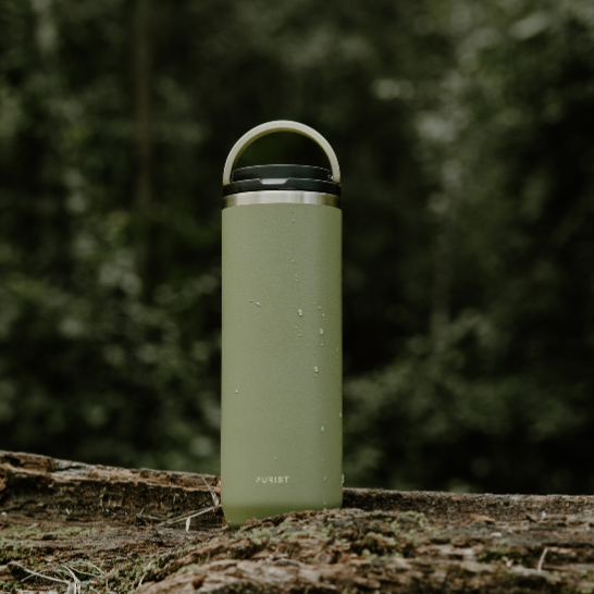 Purist stainless Green water bottle on a log with a forest background