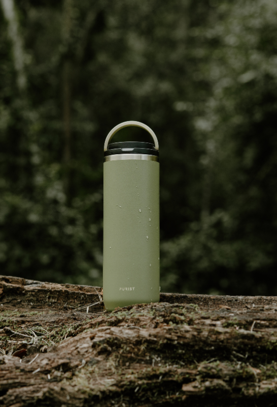 Purist stainless Green water bottle on a log with a forest background